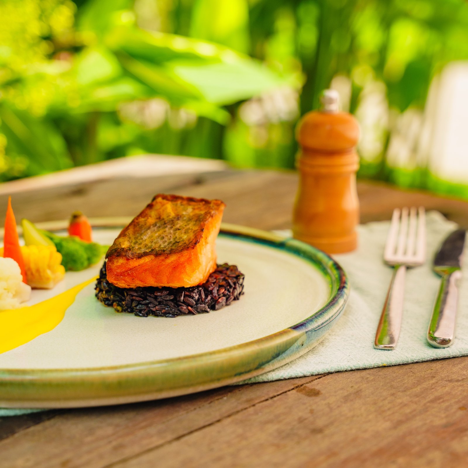 Plated salmon dish with black rice and vegetables on an outdoor table