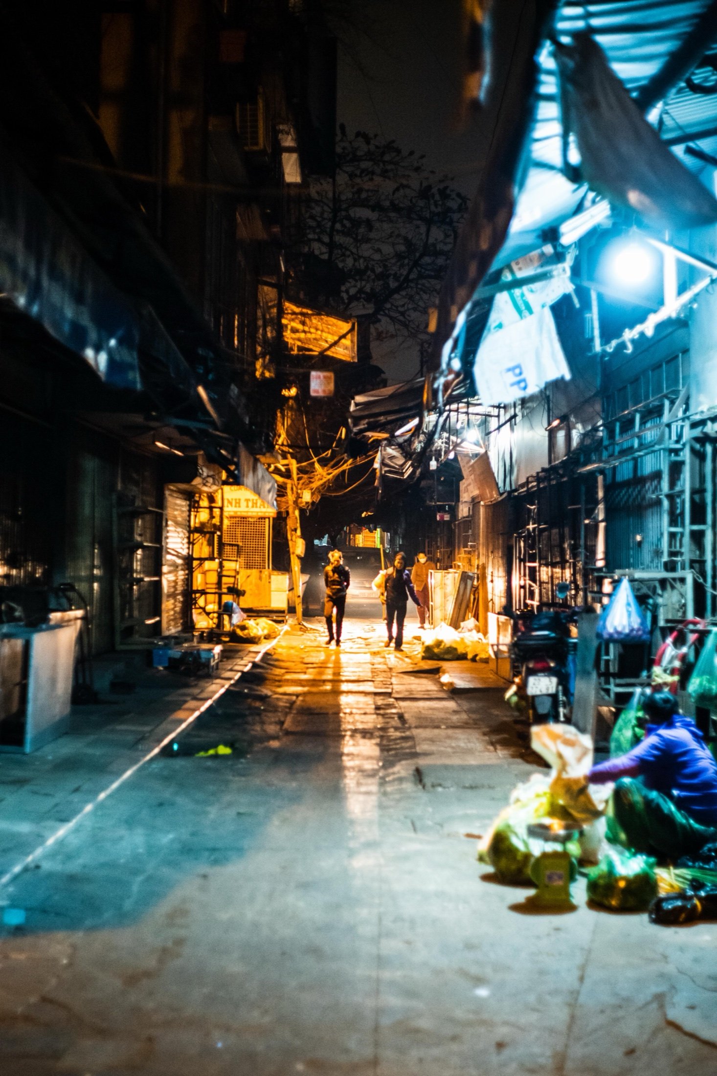 Two figures walking through a narrow night market alley lit in gold and blue
